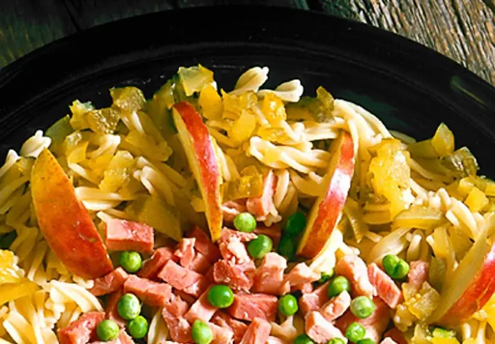 En närbild på en läcker pastasallad med skinka, äppelklyftor och gröna ärtor. En perfekt sommarmåltid!