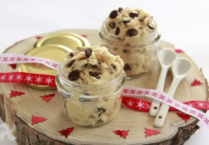 Två glasburkar fyllda med ljuvlig cookie dough, perfekt för ett enkelt cookie dough recept. Julpynt och små skedar ligger redo.