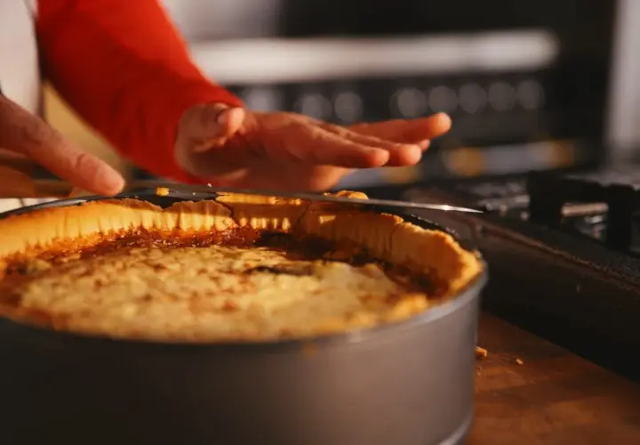 En person skär en gyllene quiche lorraine i en form. Den ser utsökt ut!