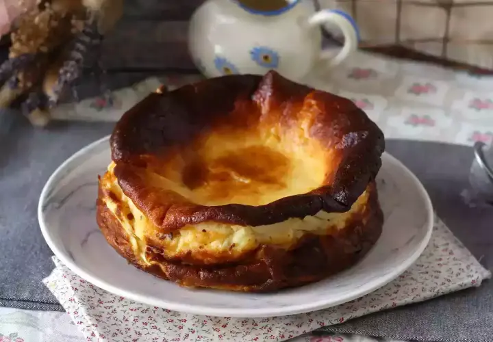 En krämig baskisk cheesecake med karamelliserad yta, serverad på en tallrik med blommig duk.