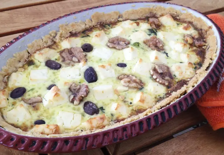 Spinach and feta quiche with walnuts and olives in a rustic tart dish.