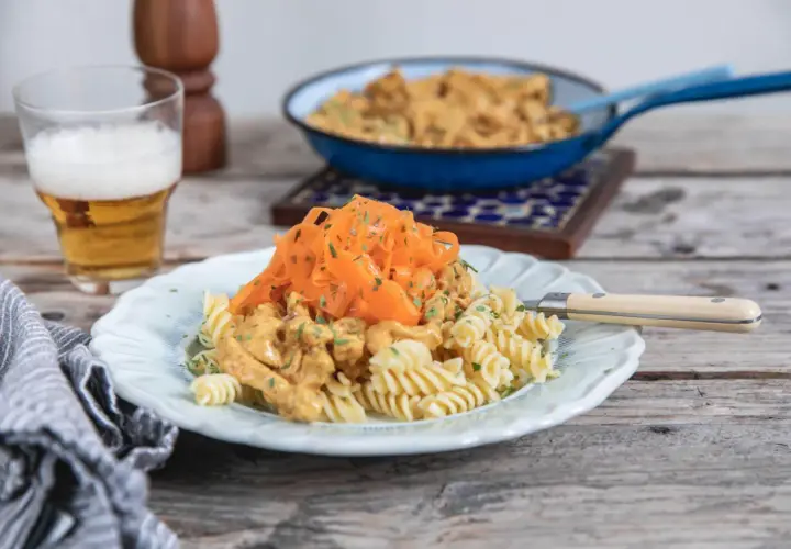 En tallrik med rotfrukter och ost och skinksås över pasta. En öl står bredvid.