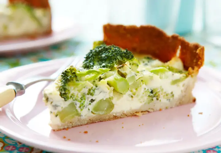 En bit broccoli och ädelostpaj på en rosa tallrik. Pajen har en gyllene botten och fyllning med broccoli och krämig ost.