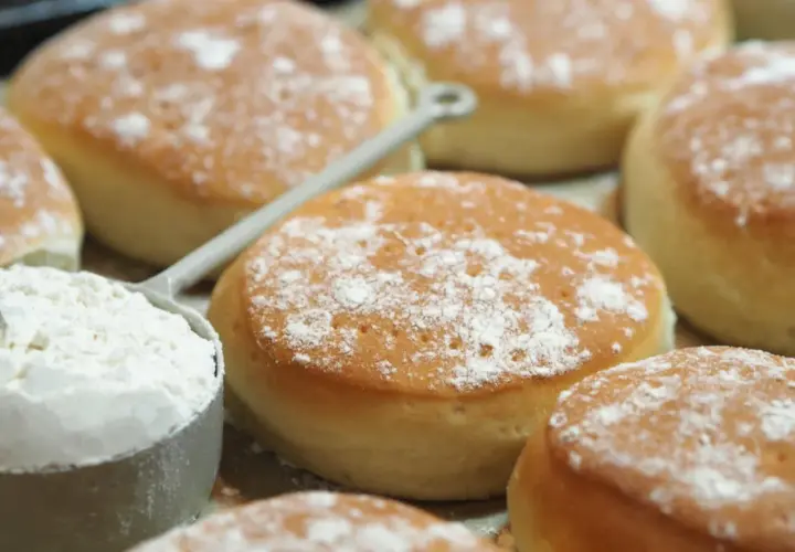 Nybakade tekakor, pudrade med mjöl, redo för ett enkelt tekakor recept. En skopa mjöl syns i förgrunden.