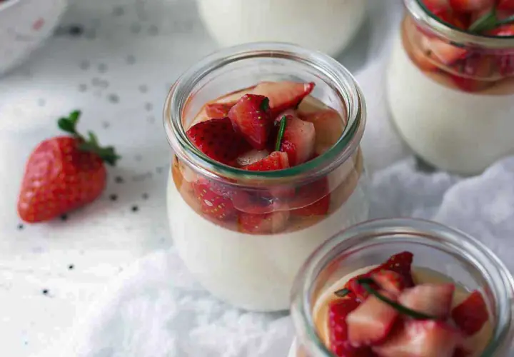 Pannacotta in glass jars topped with fresh strawberries and rosemary.