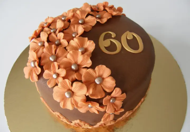 Chokladtårta med aprikosfärgade blommor och guldigt "60" som firar en 60-årig födelsedag.