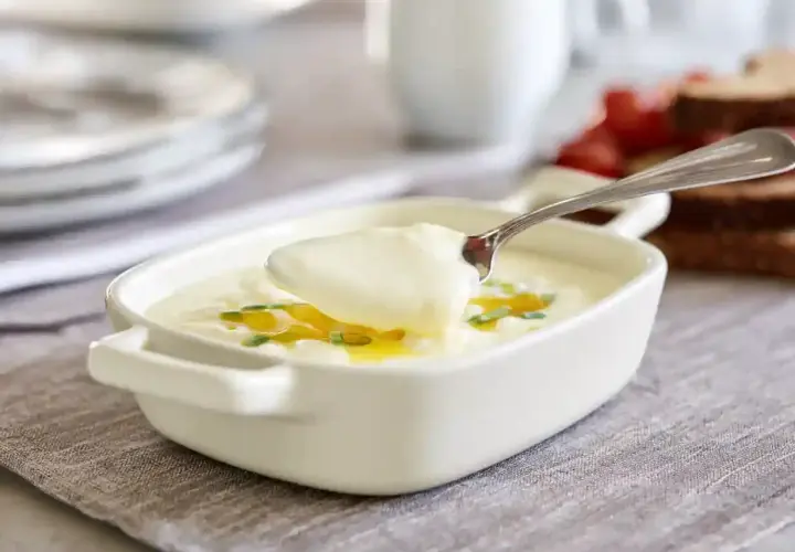 En sked lyfter krämig bechamelsås ur en vit skål, garnerad med gräslök och olja. Perfekt för ditt bechamelsås recept.