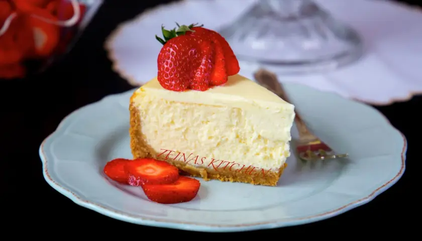 En bit krämig cheesecake med jordgubbar på en ljusblå tallrik. Undrar du hur länge håller cheesecake i kylen? Denna ser god ut!