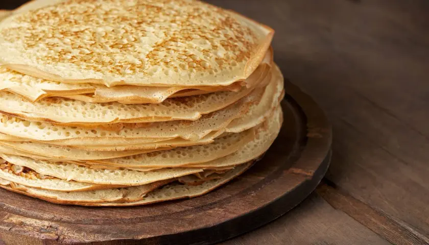 En hög med gyllene pannkakor, perfekt för ett gott pannkakssmet recept. De ligger på en mörk träskärbräda.