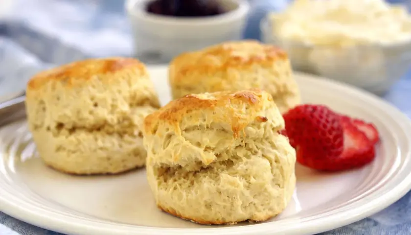 Tre gyllene scones på en vit tallrik, redo att avnjutas med sylt och grädde. Ett perfekt scones recept för fikat.