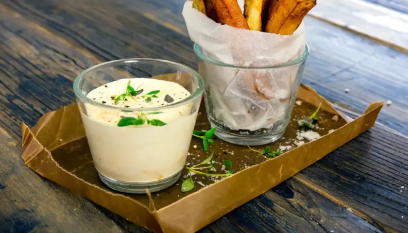 En krämig sås med creme fraiche, toppad med örter, bredvid ett glas med krispiga pommes frites.
