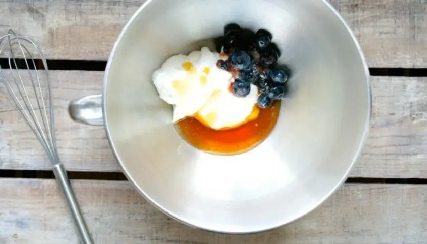 En skål med yoghurt, honung och blåbär, redo att vispas till en härlig frozen yoghurt. En visp ligger bredvid.