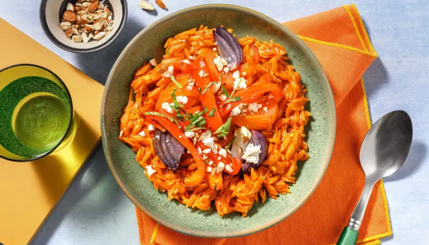 En skål med orzo pasta med rostade grönsaker och fetaost, perfekt för medelhavskost recept. Toppad med mandlar och färska örter.