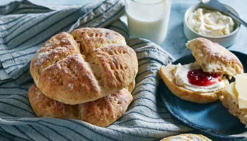 Nybakade scones med sylt och grädde, serverade med ett glas mjölk. Perfekt för en mysig fika.