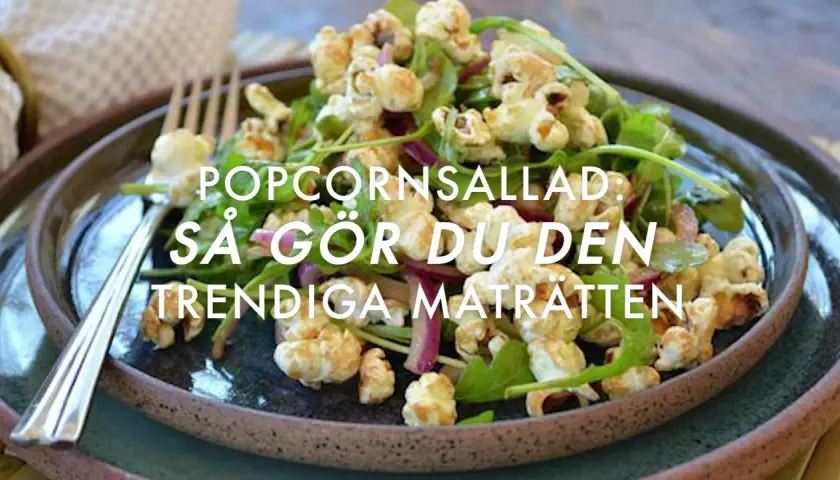 A close-up of a popcorn salad with greens and red onion on a dark plate, with a fork.