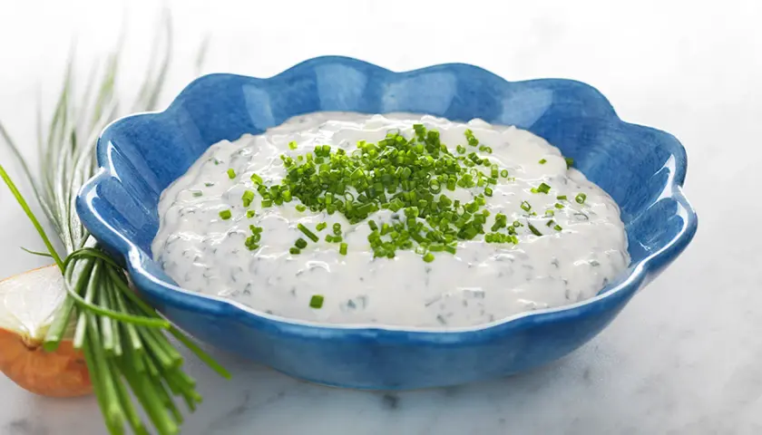 Kall sås till paj, en krämig gräddfilssås med gräslök, serverad i en blå skål.