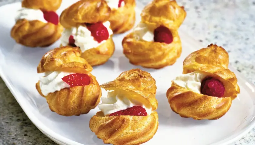 Cream puffs filled with whipped cream and topped with raspberries and strawberries on a white platter.