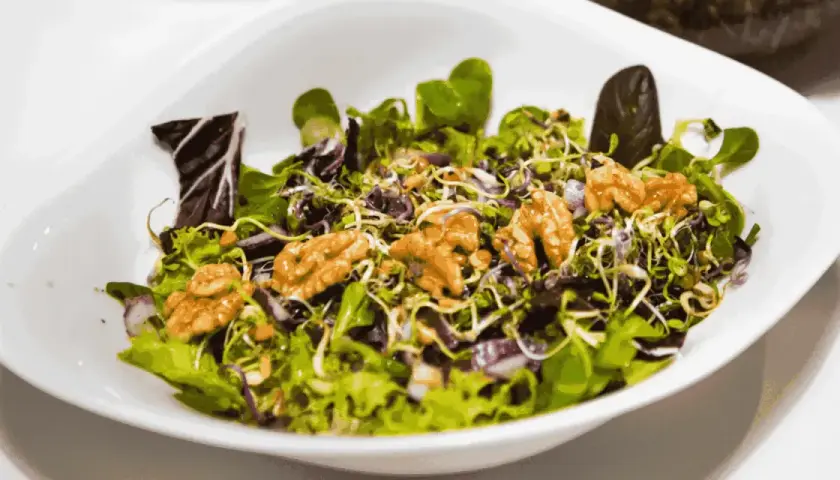 A fresh salad with mixed greens, sprouts, red onion, and walnuts in a white bowl.