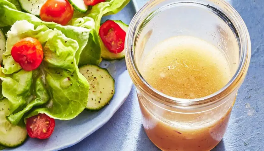 En burk med gyllene dressing till sallad står bredvid en fräsch sallad med gurka och tomater.