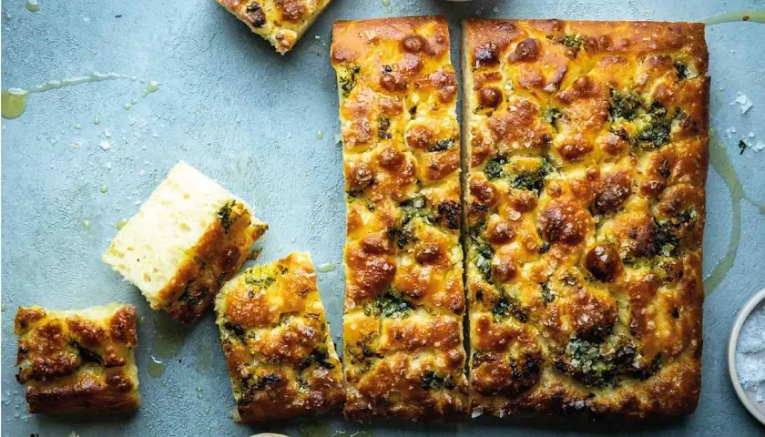 En gyllene focaccia långpanna med örter och flingsalt, uppskuren och redo att avnjutas.