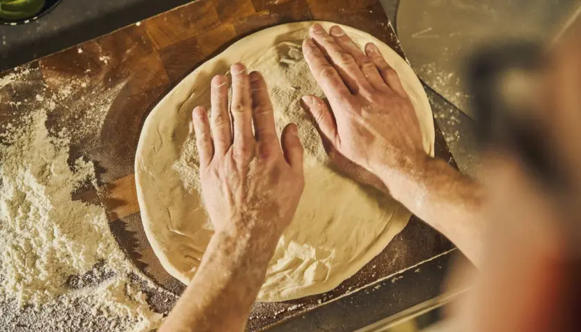 Händer formar pizzadeg på en skärbräda med mjöl. Ett steg i ett klassiskt pizza recept.