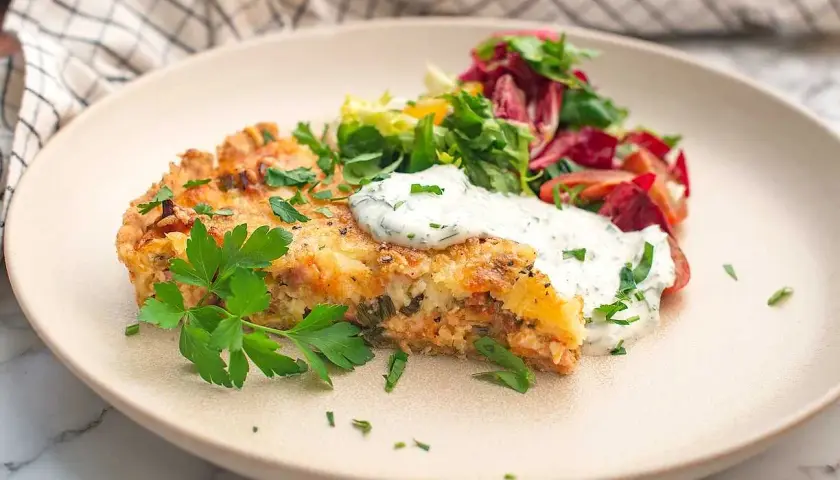 En bit saftig skinkpaj utan ost, toppad med färska örter och en klick krämig sås, serveras med en fräsch sallad.