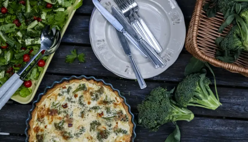 En gyllene västerbottenpaj med broccoli, en fräsch sallad och färsk broccoli i en korg. En härlig måltid!