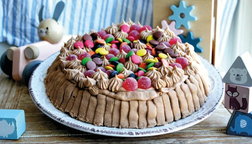 En härlig glutenfri tårta dekorerad med chokladfrosting och färgglada godisar, perfekt för barnkalas.