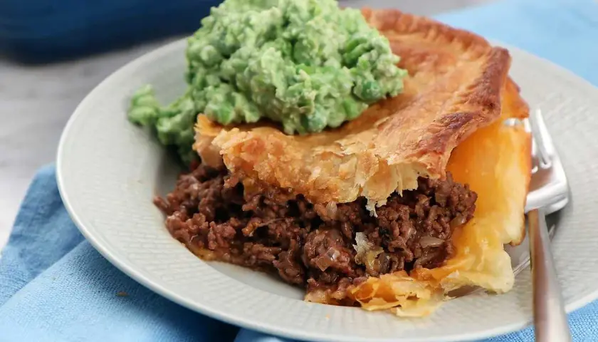 En bit köttfärspaj utan äggstanning med en klick grön mos på en tallrik.