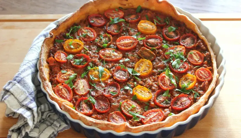 En gyllene köttfärspaj med körsbärstomater och färska örter, redo att serveras.