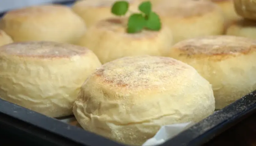 En bricka med nybakade, gyllene english muffins, redo att delas och njutas. En liten grön kvist vilar på en av dem.