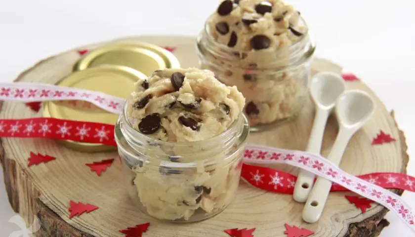 Två glasburkar fyllda med ljuvlig cookie dough, perfekt för ett enkelt cookie dough recept. Julpynt och små skedar ligger redo.