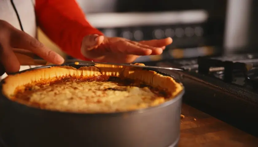 En person skär en gyllene quiche lorraine i en form. Den ser utsökt ut!