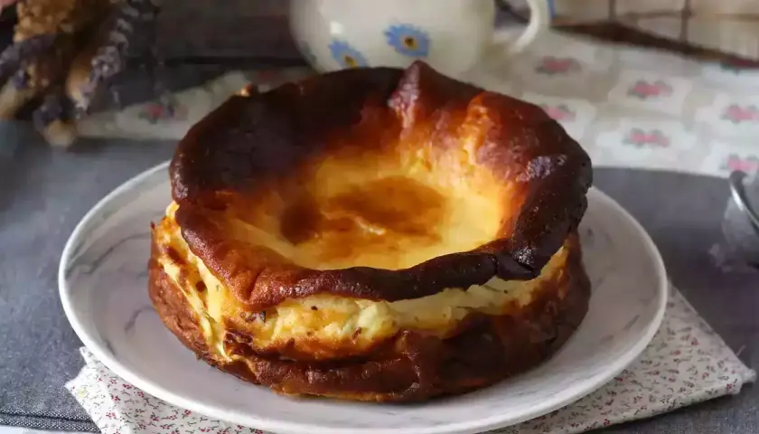 En krämig baskisk cheesecake med karamelliserad yta, serverad på en tallrik med blommig duk.