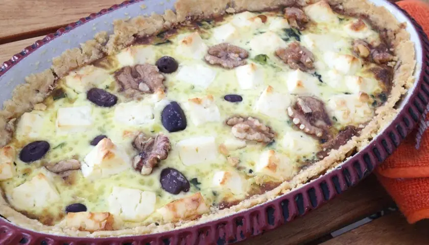 Spinach and feta quiche with walnuts and olives in a rustic tart dish.