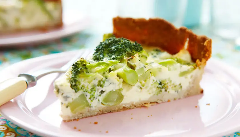 En bit broccoli och ädelostpaj på en rosa tallrik. Pajen har en gyllene botten och fyllning med broccoli och krämig ost.