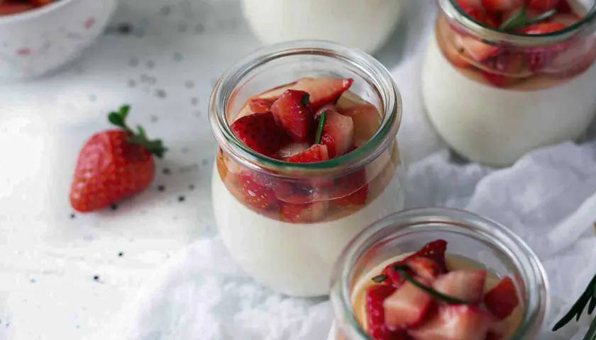 Pannacotta in glass jars topped with fresh strawberries and rosemary.