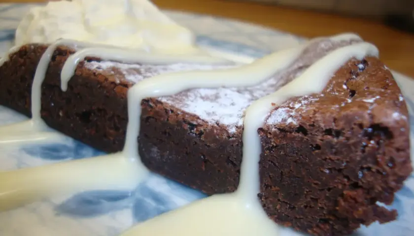 En saftig kladdkaka med sirap, pudrad med florsocker och toppad med vispad grädde.