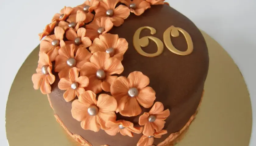 Chokladtårta med aprikosfärgade blommor och guldigt "60" som firar en 60-årig födelsedag.