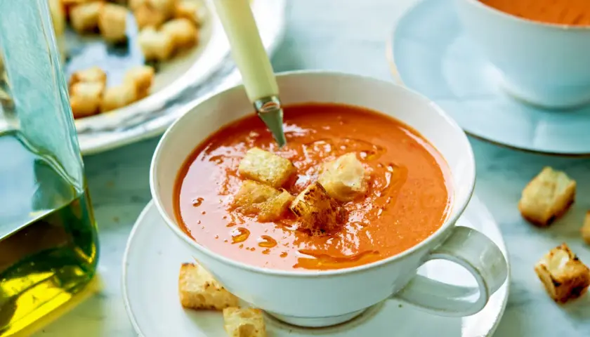 En skål med gazpacho, toppad med krutonger. Bredvid en karaff med olivolja. Ett perfekt gazpacho recept för en varm dag.