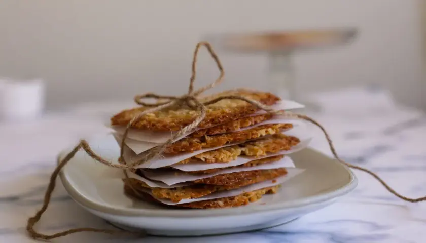 Stack of thin, golden-brown oat cookies tied with twine on a white plate.