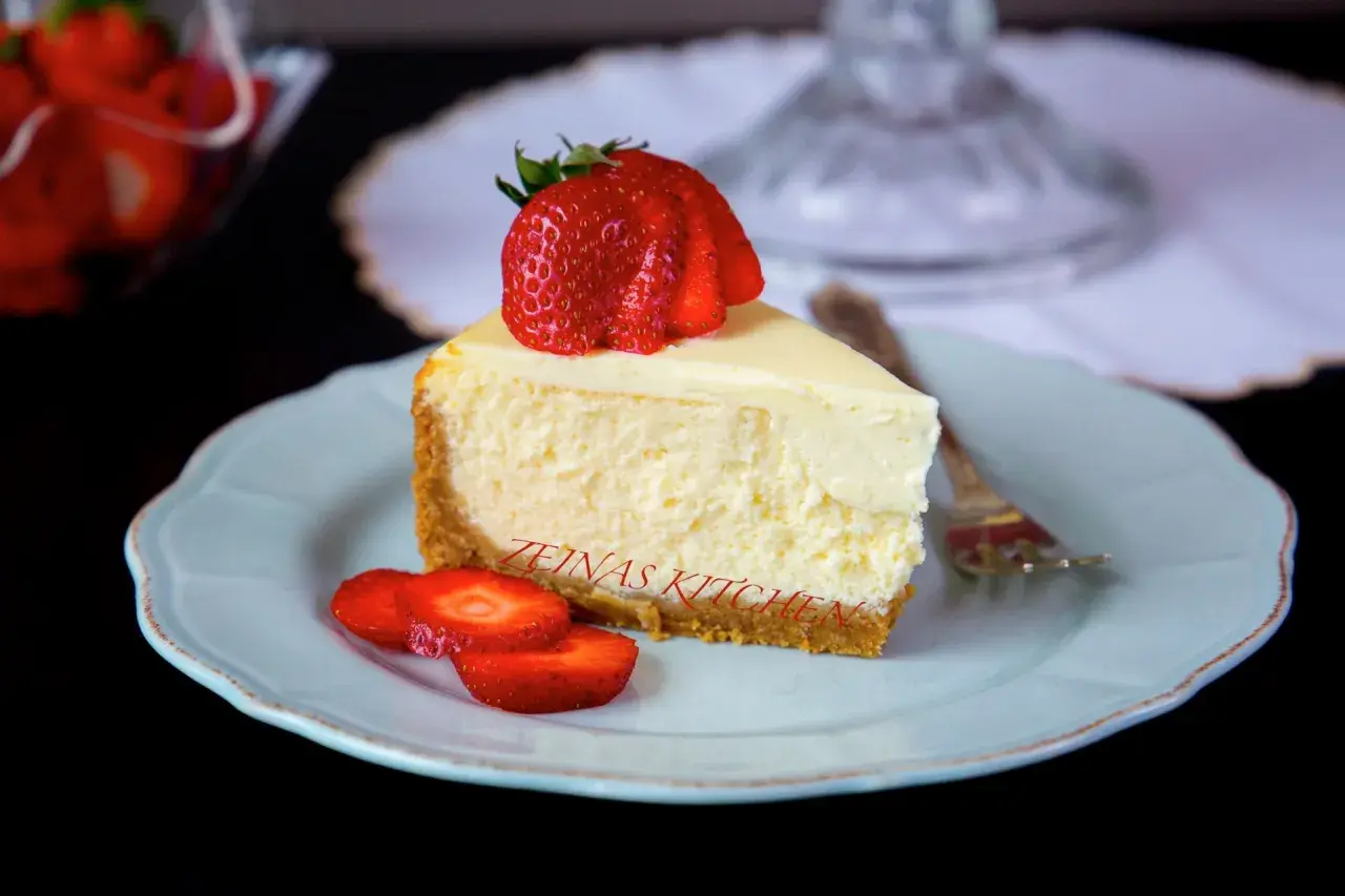 En bit krämig cheesecake med jordgubbar på en ljusblå tallrik. Undrar du hur länge håller cheesecake i kylen? Denna ser god ut!