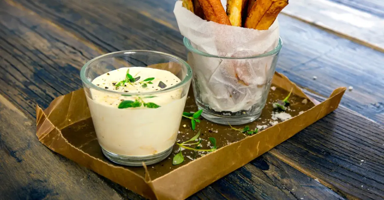 En krämig sås med creme fraiche, toppad med örter, bredvid ett glas med krispiga pommes frites.