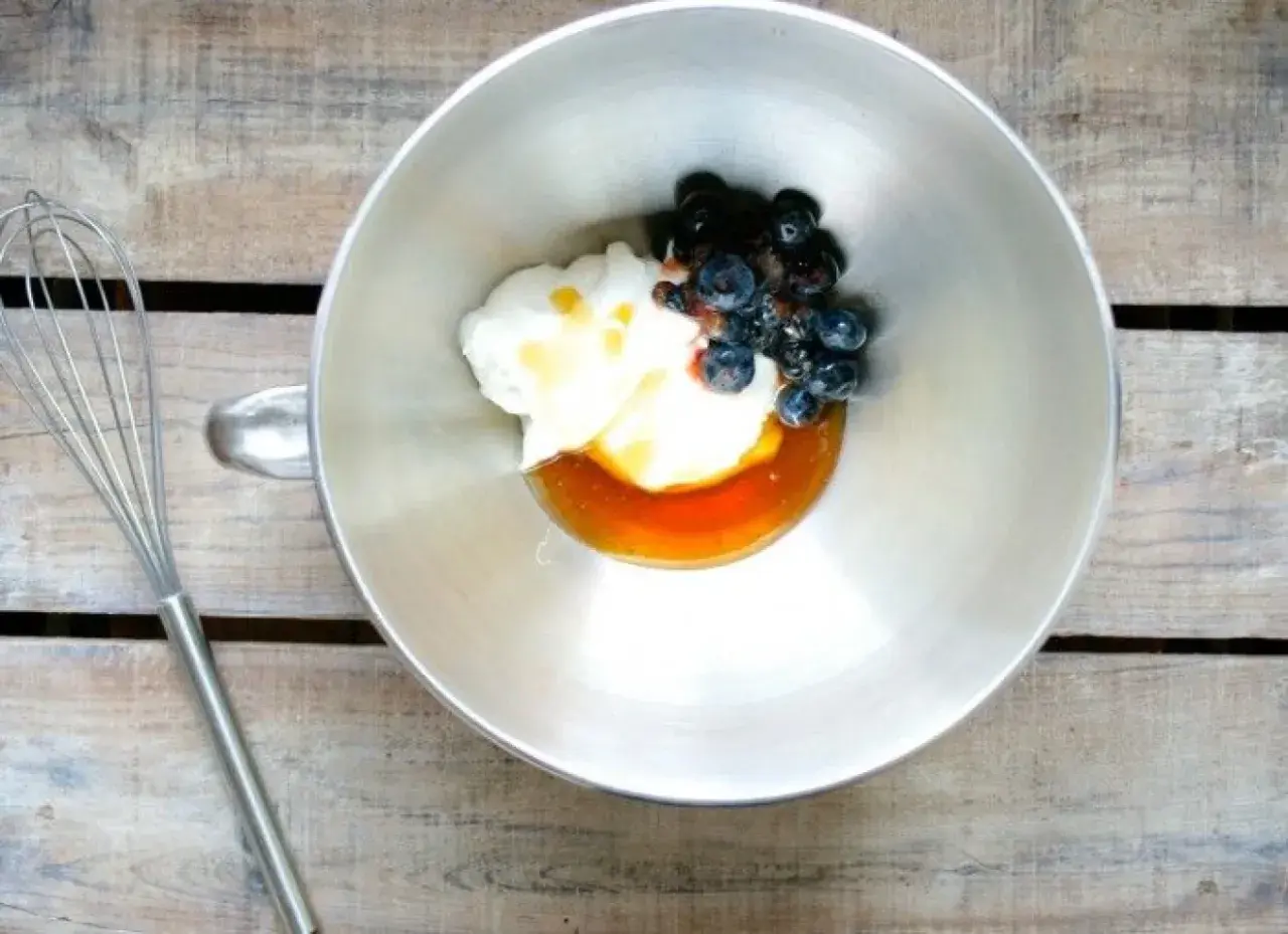 En skål med yoghurt, honung och blåbär, redo att vispas till en härlig frozen yoghurt. En visp ligger bredvid.