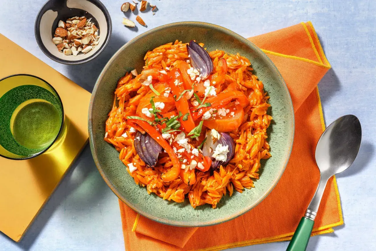 En skål med orzo pasta med rostade grönsaker och fetaost, perfekt för medelhavskost recept. Toppad med mandlar och färska örter.
