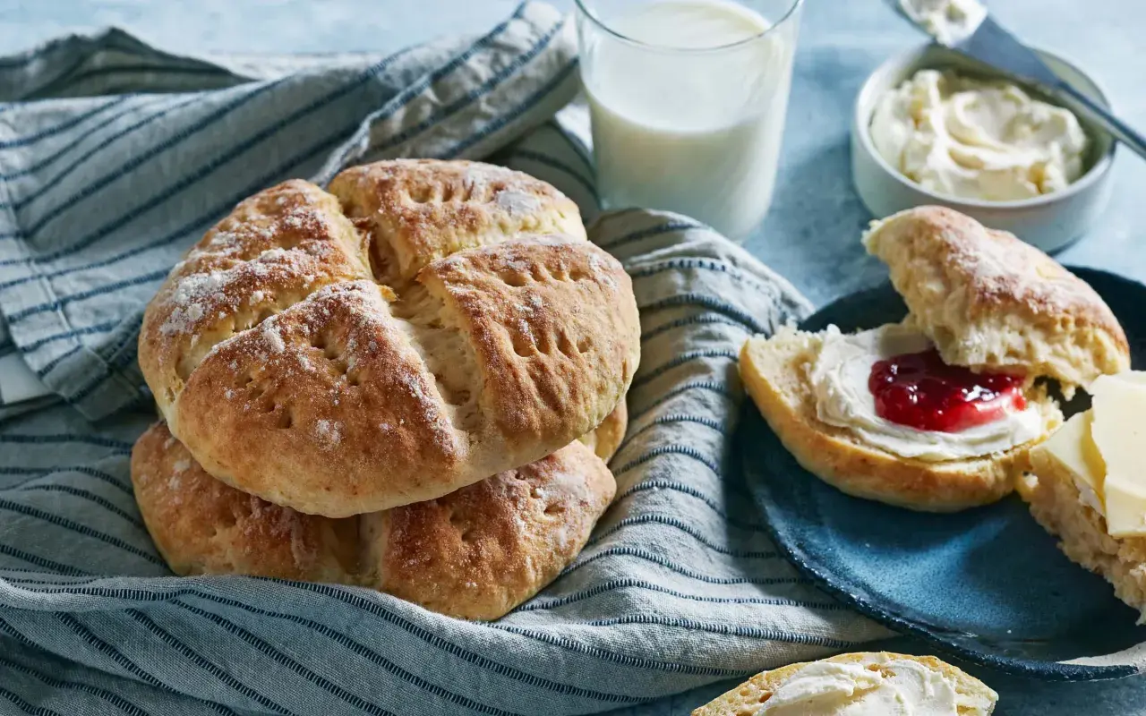 Nybakade scones med sylt och grädde, serverade med ett glas mjölk. Perfekt för en mysig fika.
