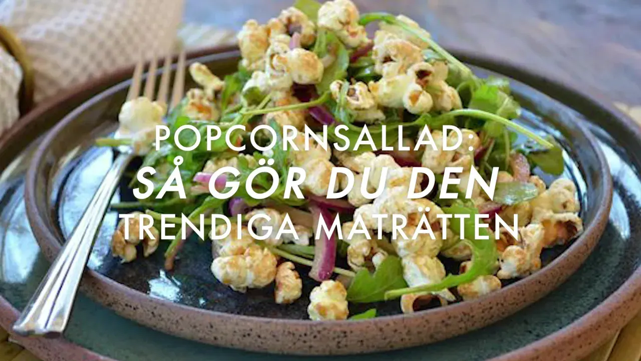 A close-up of a popcorn salad with greens and red onion on a dark plate, with a fork.