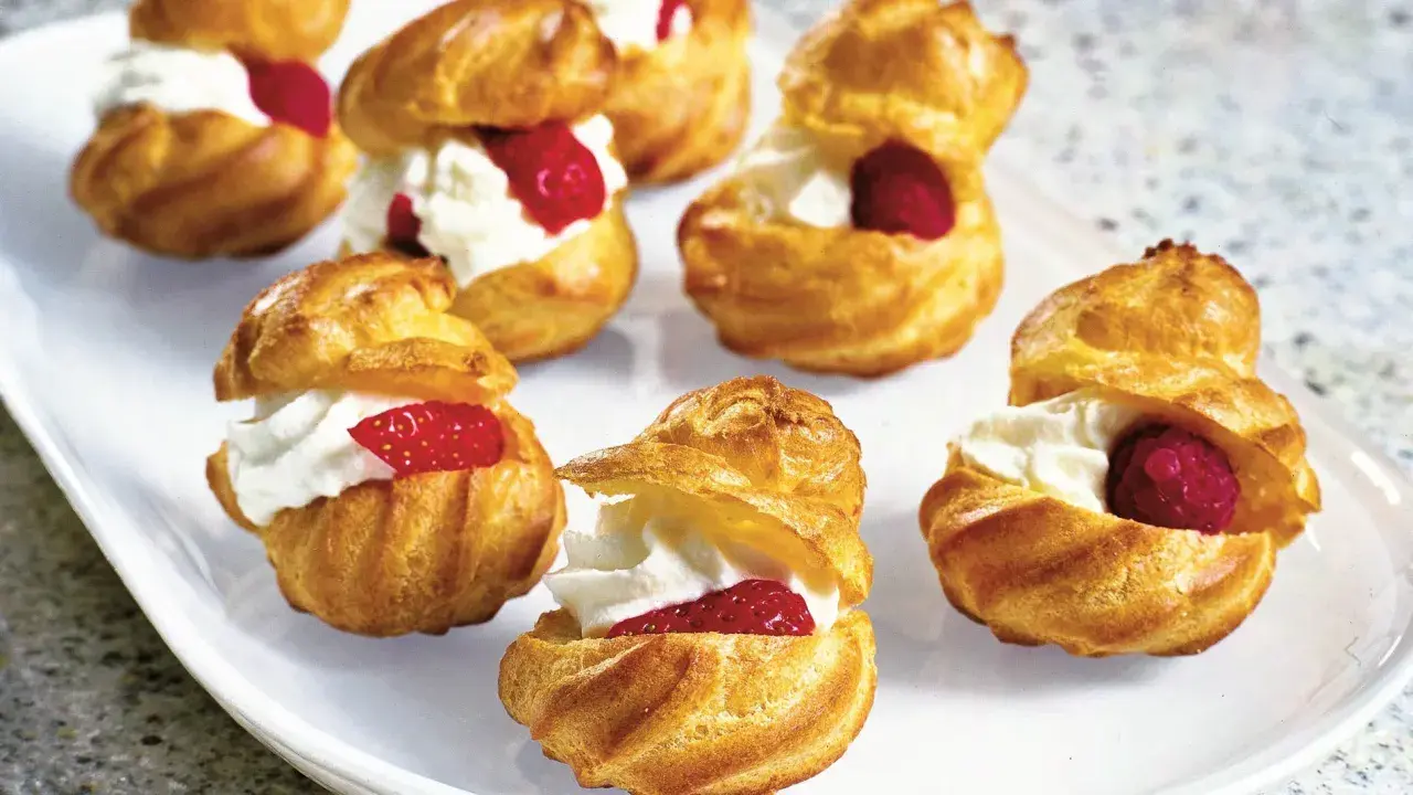 Cream puffs filled with whipped cream and topped with raspberries and strawberries on a white platter.