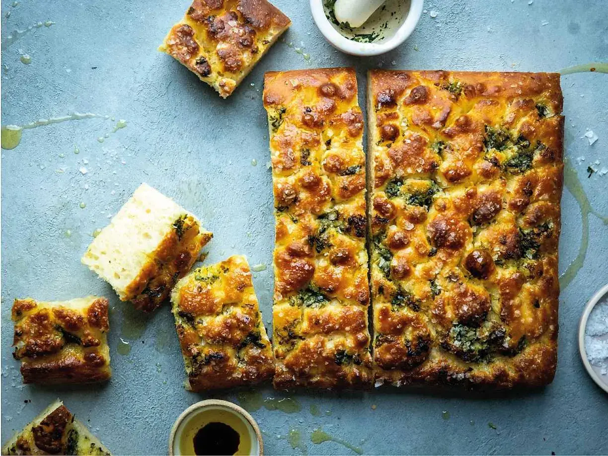 En gyllene focaccia långpanna med örter och flingsalt, uppskuren och redo att avnjutas.