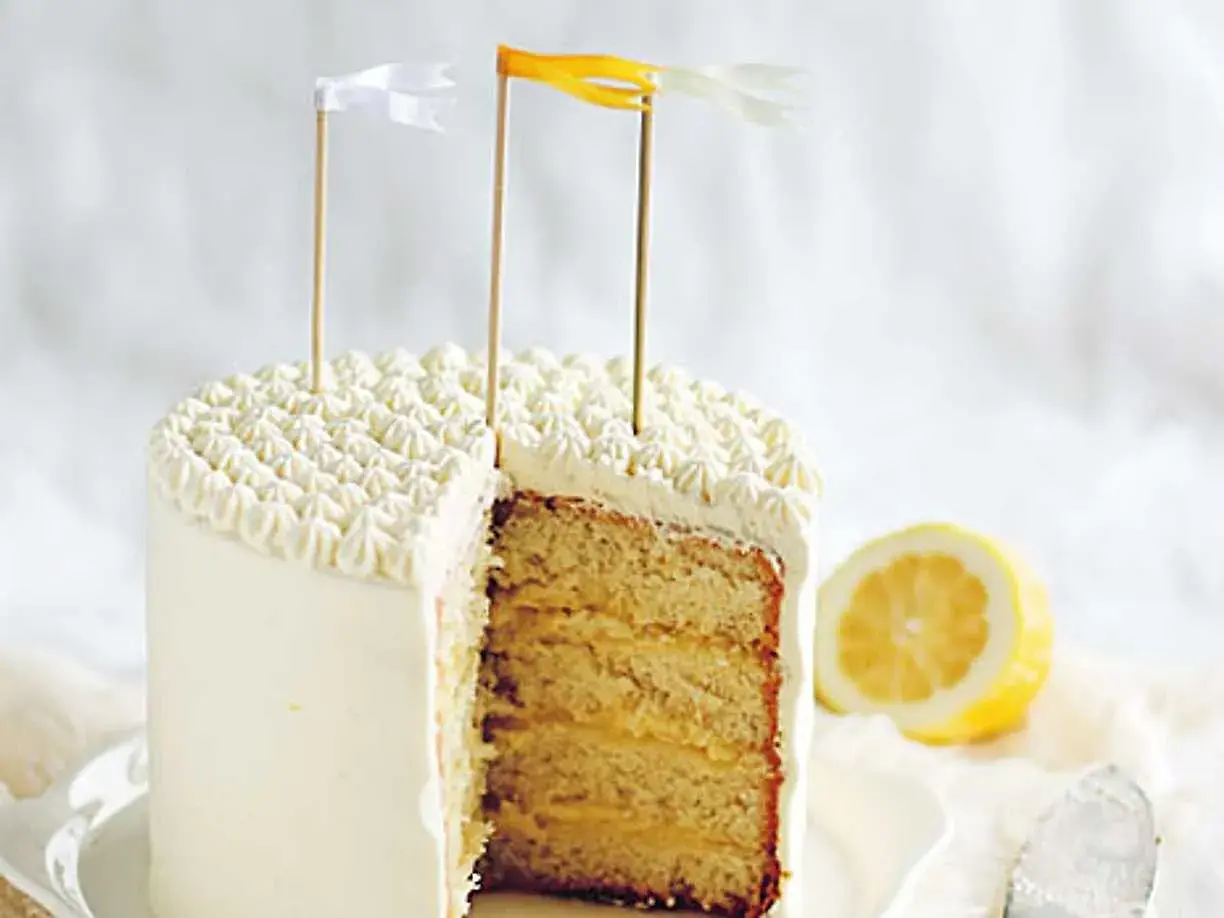 Tårta med fluffig frosting och lager av saftig sockerkaka fylld med syrlig lemon curd. En citronskiva ligger bredvid.